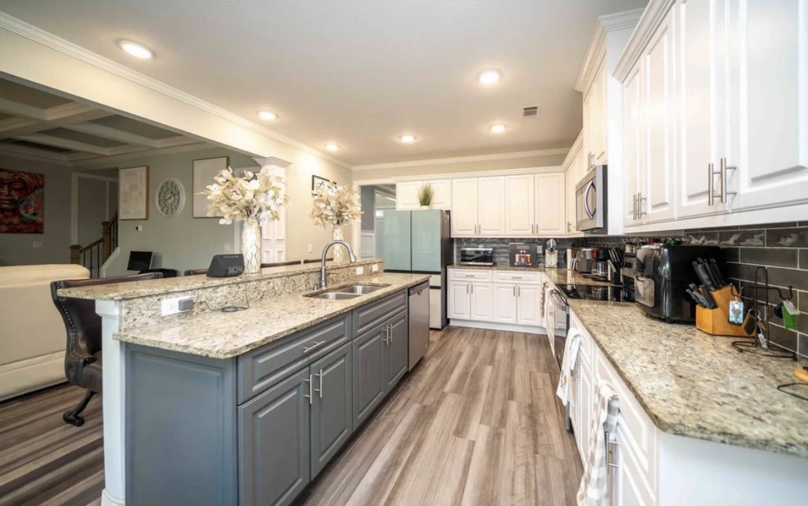Kitchen with white cabinets, granite island with sink and stainless appliances
