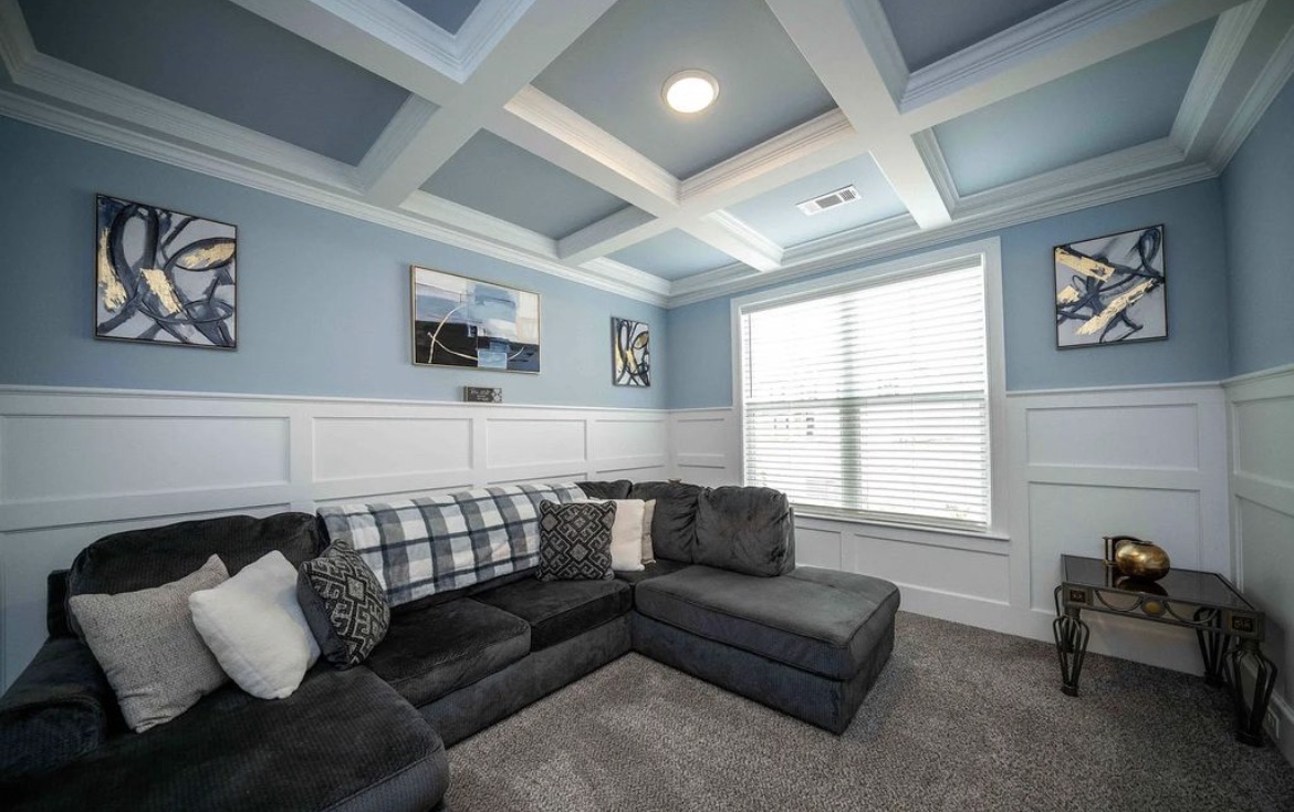 Blue den with coffered ceiling, wainscoting, grey sectional and framed abstract art