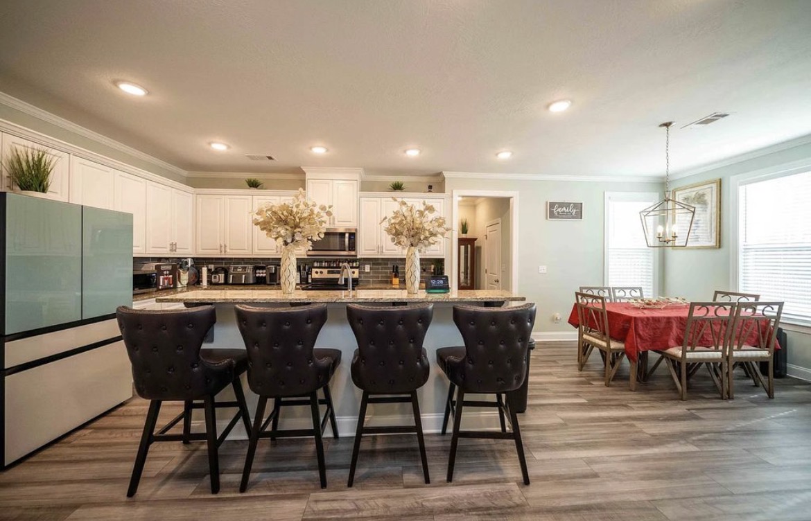 Granite island with four tufted leather bar stools beside a breakfast table