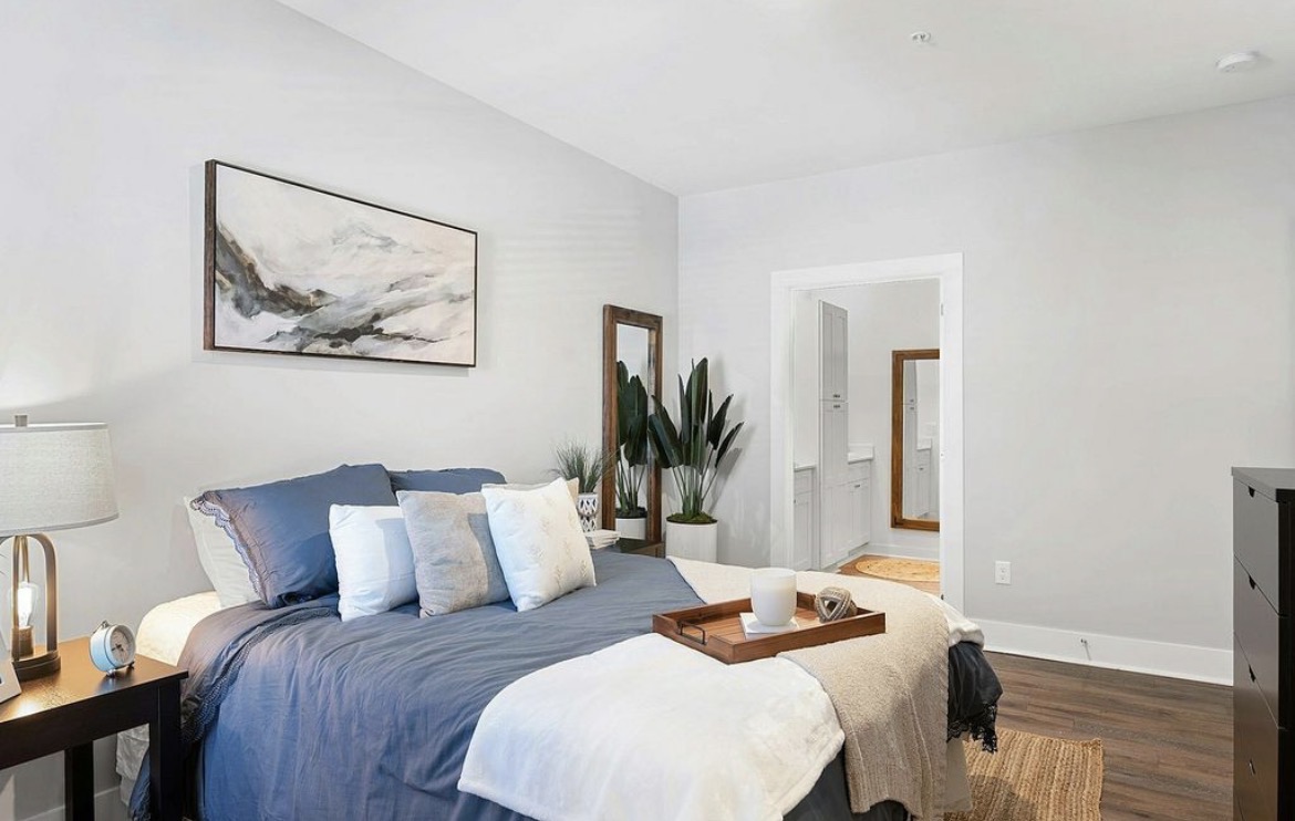 Bedroom with queen bed, blue linens, leaning mirror and en-suite bath entry