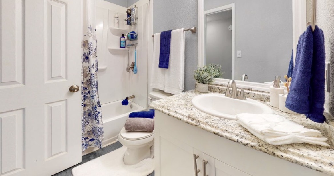 Bathroom with granite vanity, large mirror, shower-tub combo and navy towels