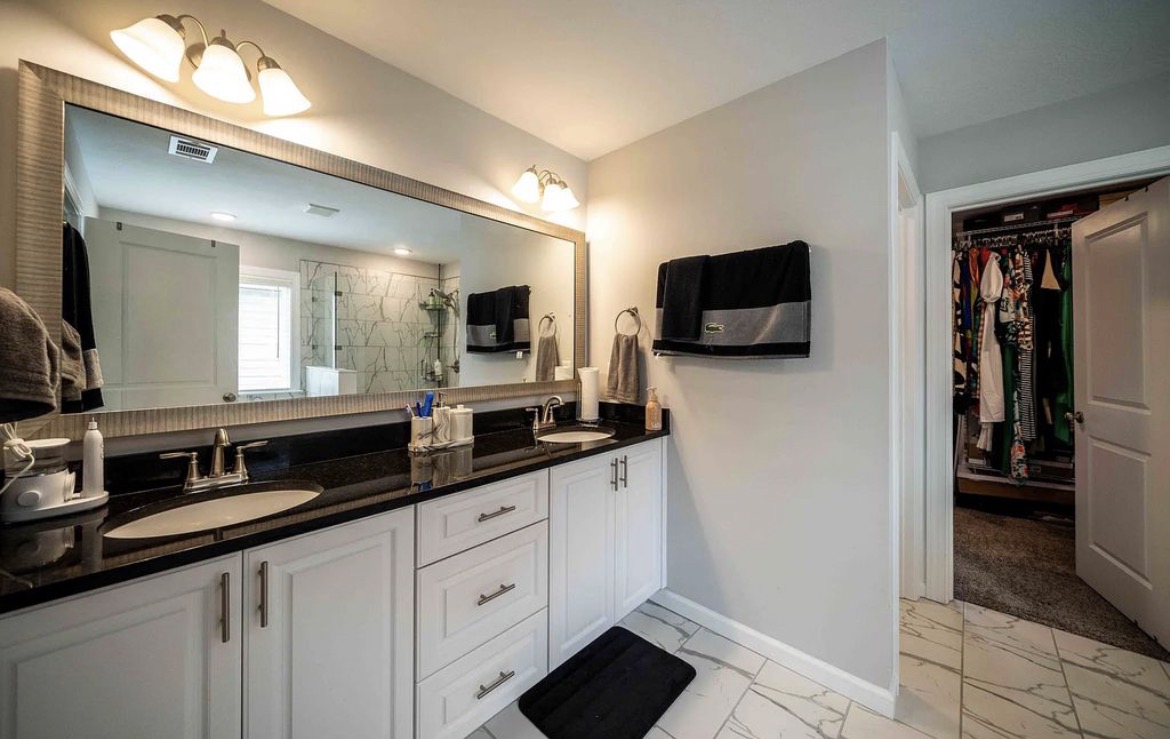 Primary bathroom with double granite vanity, large mirror and walk-in closet