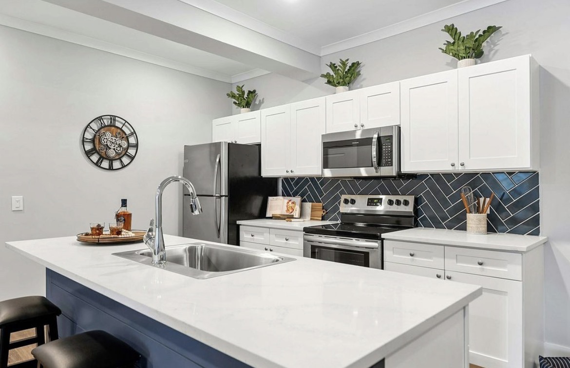 Kitchen with white shaker cabinets, navy herringbone backsplash and quartz island sink