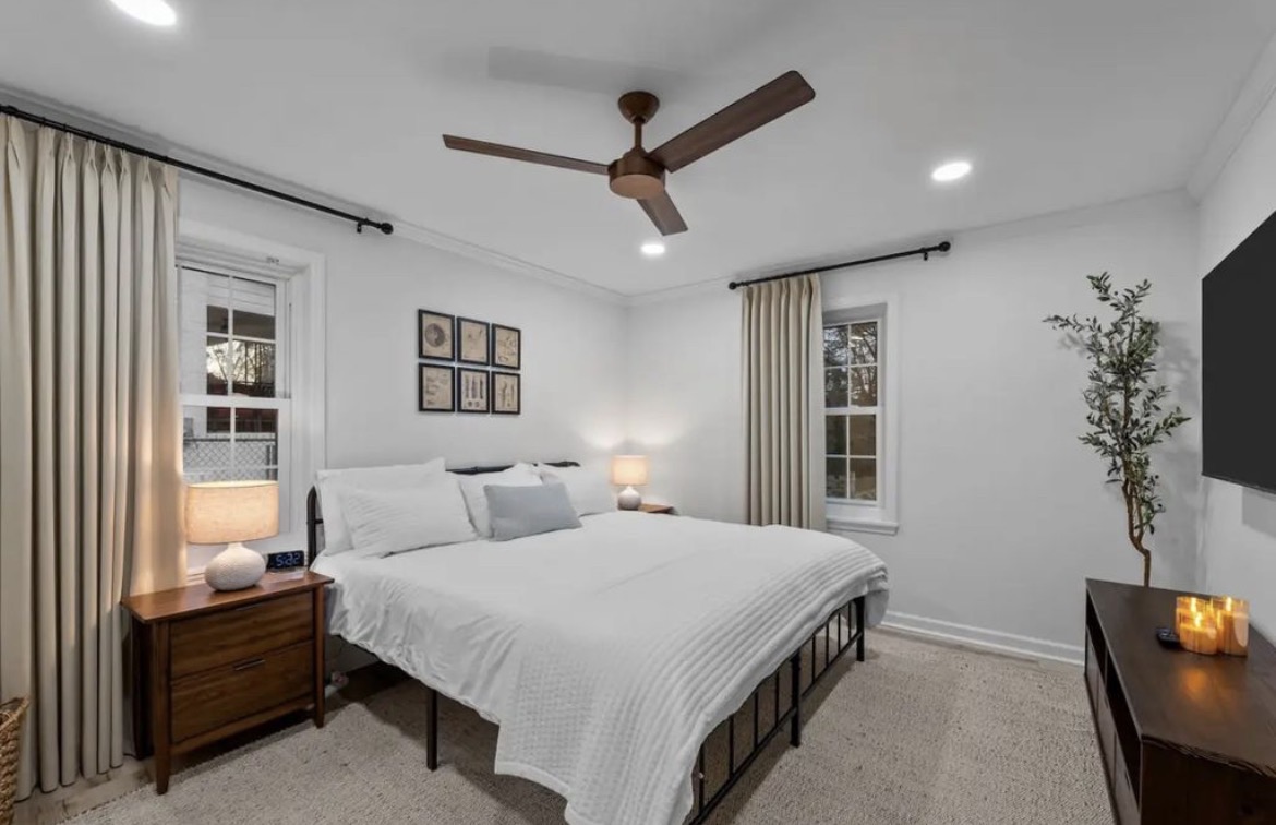 Primary bedroom with king bed, white linens, ceiling fan and wall-mounted TV