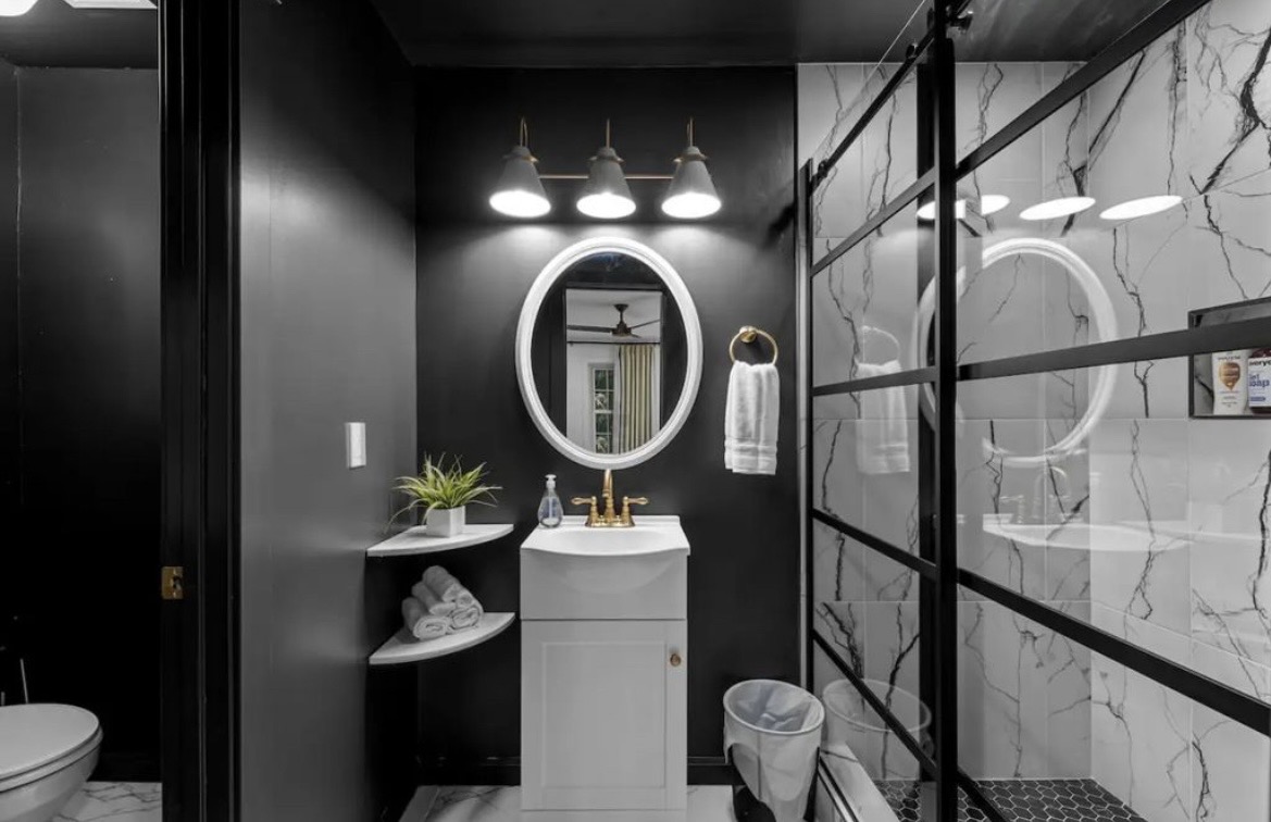 Bathroom with black walls, oval mirror, gold fixtures and marble-tiled glass shower