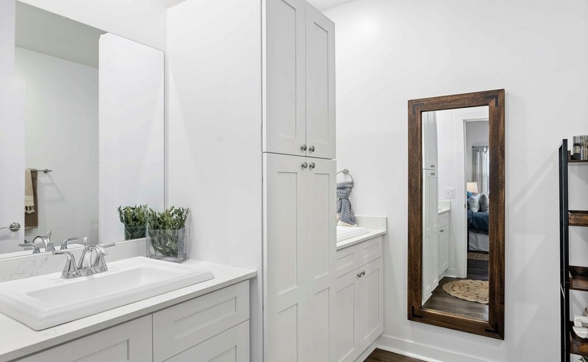Bright bathroom with white quartz vanity, tall linen cabinet and wood framed mirror