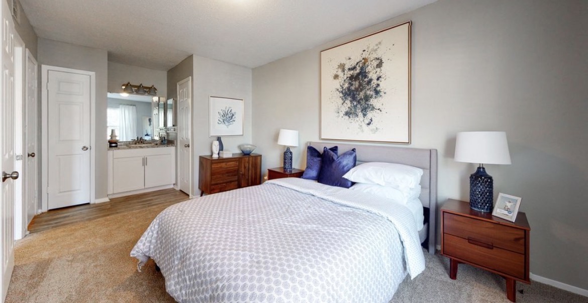 Bedroom with queen bed, navy accent pillows, wood nightstands and en-suite vanity