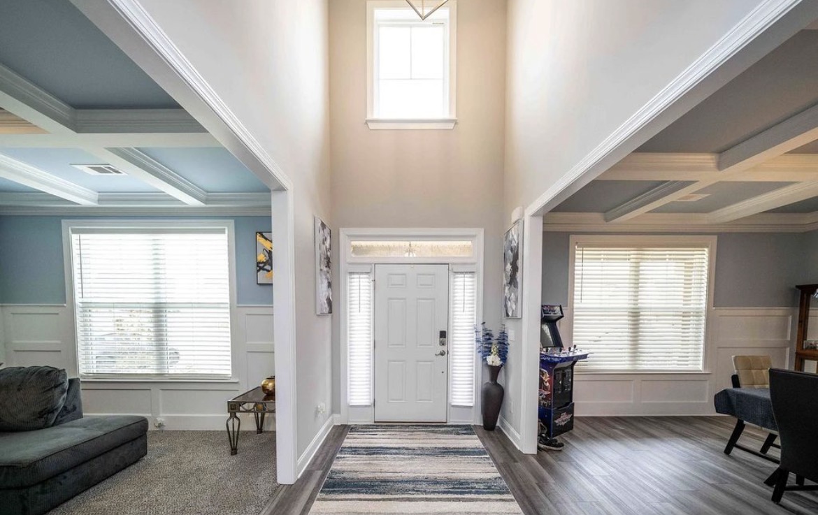 Two-story entry foyer with white front door, runner rug and rooms on either side