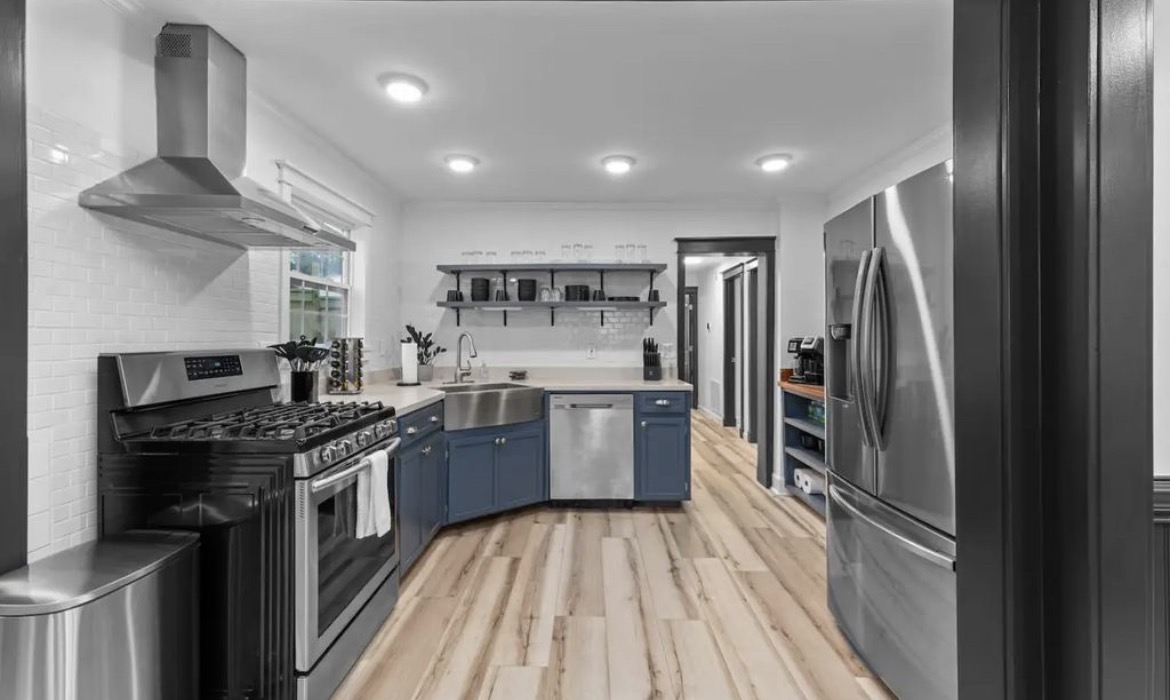 Galley kitchen with blue cabinets, stainless gas range, farmhouse sink and open shelving