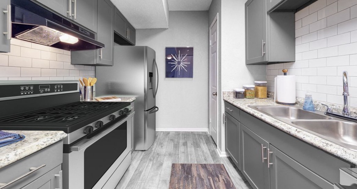 Galley kitchen with grey cabinets, granite counters, gas range and stainless refrigerator
